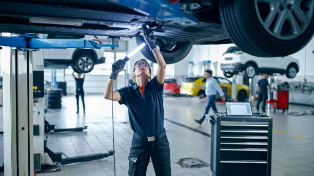 mécanicienne avec lumière travaillant sous la voiture dans un atelier de réparation automobile - garages photos et images de collection
